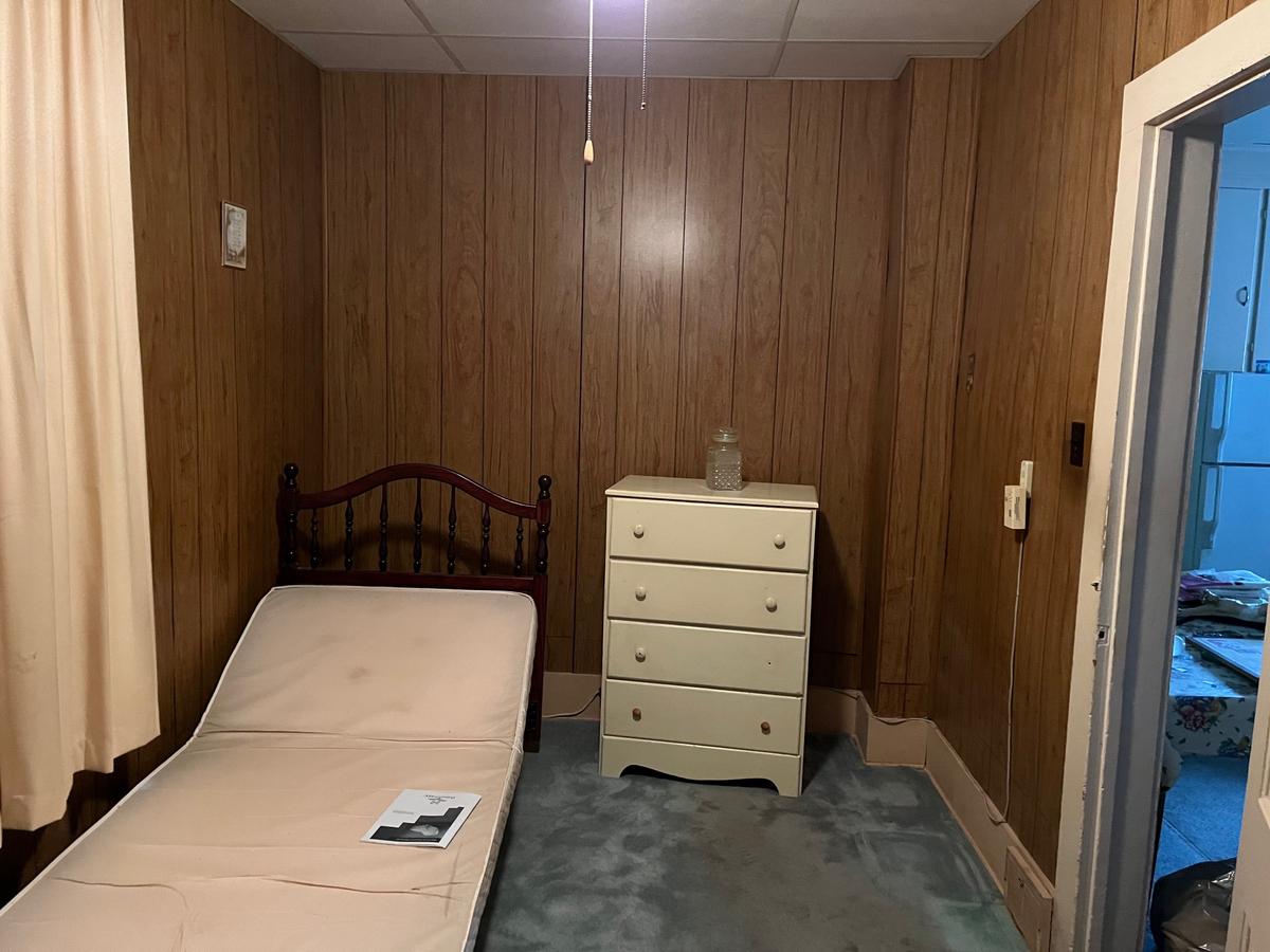 Erie NY bedroom — wood paneling throughout, original bed and dresser, single bulb lighting