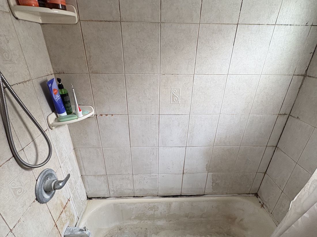 Original second-floor bathroom with dated wall tile and tub, requiring complete replacement