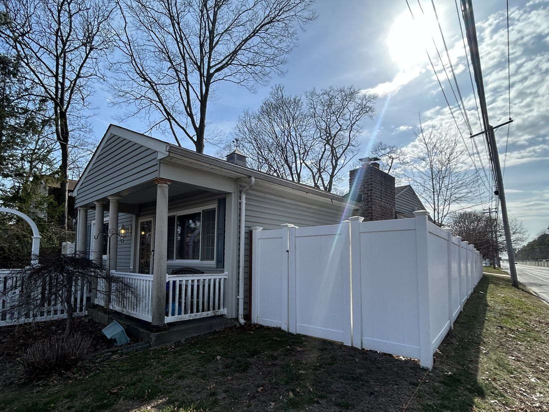 Side elevation of the West Babylon, NY home showing the vinyl privacy fence along the property line