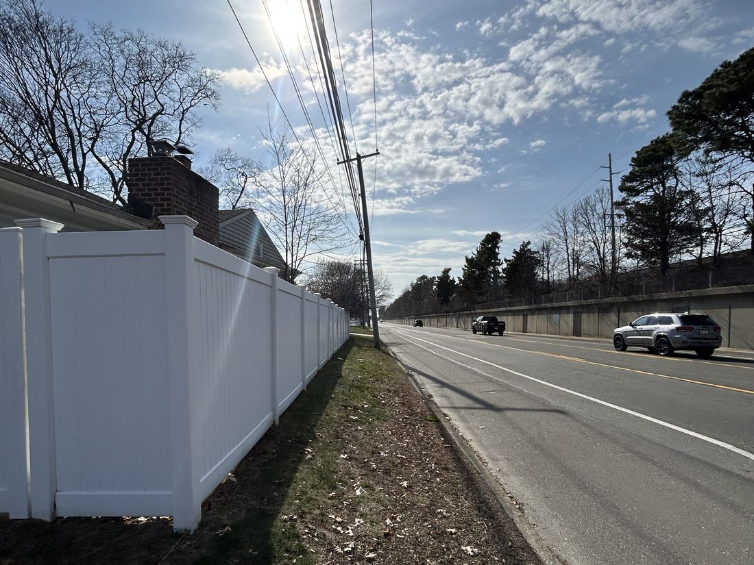 Vinyl privacy fence separating the West Babylon property from the multi-lane roadway running alongside it